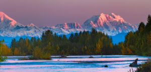 sunrise on snowcapped mountains over a lake and forrest in Alaska